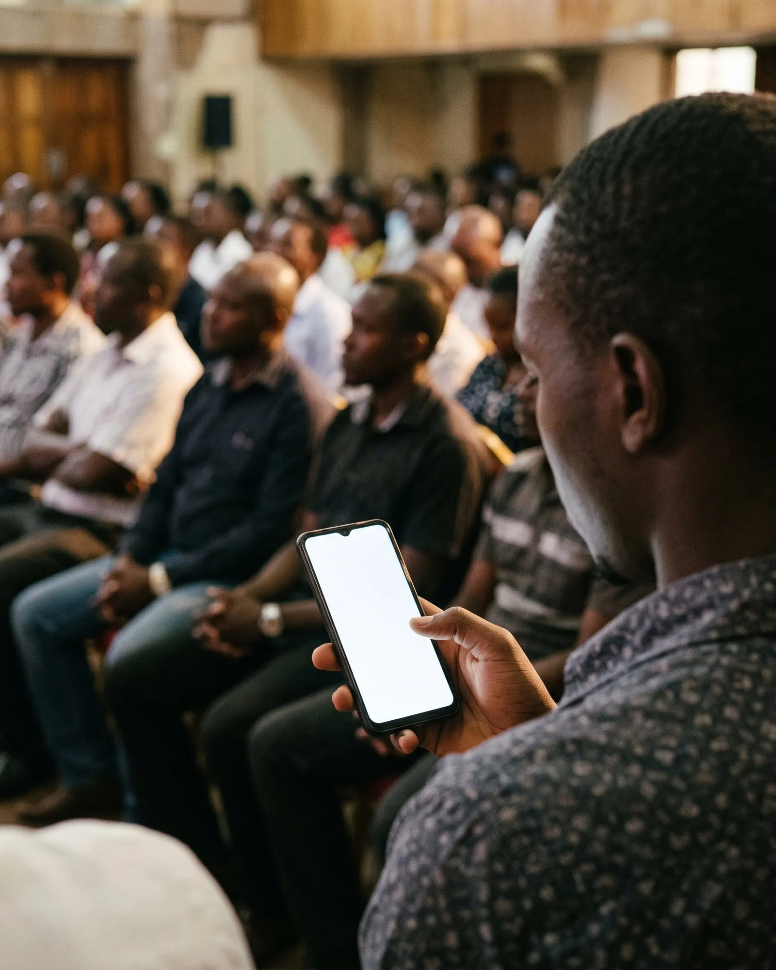 A man in an audience holds his phone and answers a Roomwave poll